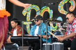 Three musicians dressed in colourful shirts play different types of drums on stage.