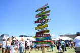 A signpost made of various pieces of driftwood nailed to a pole. Each piece of wood has a different Pacific nation painted on it, in the colours of the country's flag.