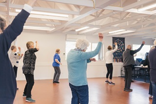 Elderly people raising their right arms, doing group exercise in a hall.