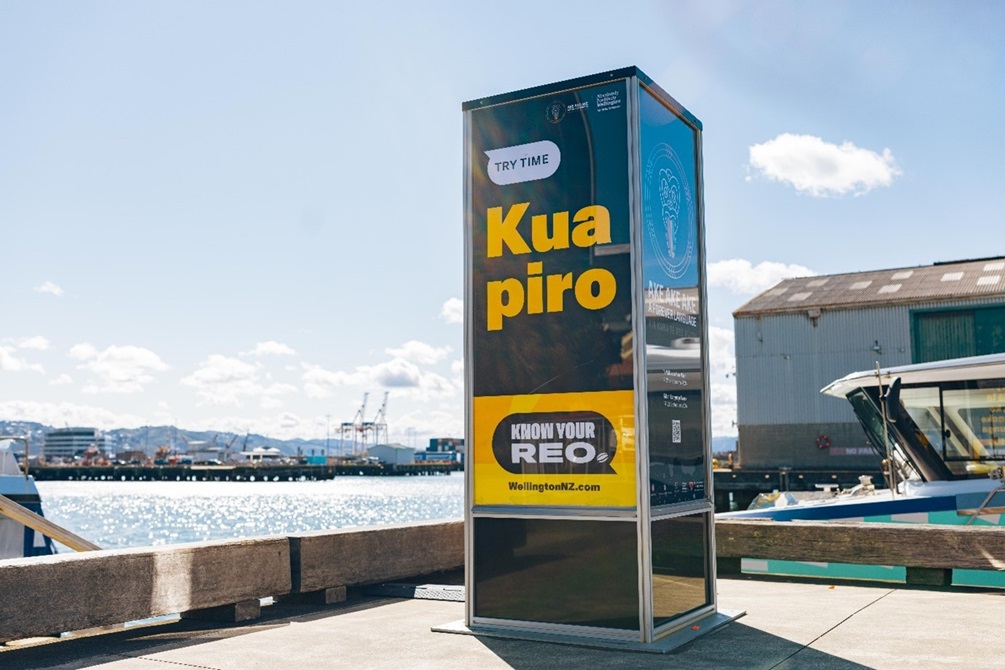 A light pou on the Wellington waterfront with a te reo Māori phrase “Kua piro” written on it, and the English translation “Try time”.