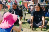A group of people of various ages playing a game involving holding two wooden sticks.