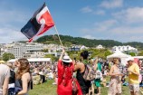 A couple in the event crowd wave a red, white and black Tino Rangatiratanga flag against a blue sky.