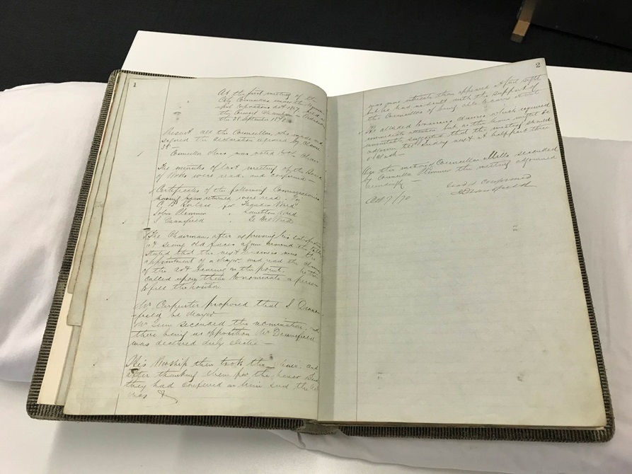 An old book opened up on a table, showing meeting minutes.