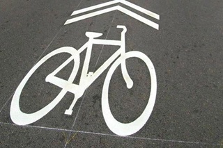A white cycle symbol with two white chevron markings above it on a road surface.