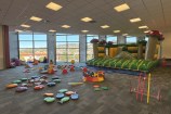 A bouncy castle surrounded by soft obstacles and colourful toys for small children, set up inside a room.