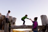 A child balancing across a raised log, helped by a caregiver.