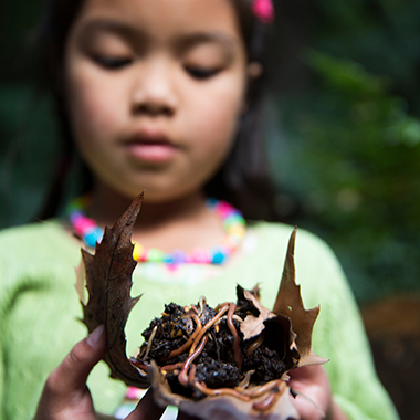 Young girl holding a leaf with soil and worms.