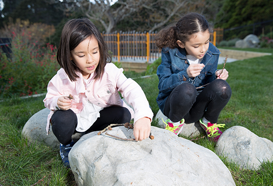 Two young girls arranging sticks on top a stone.