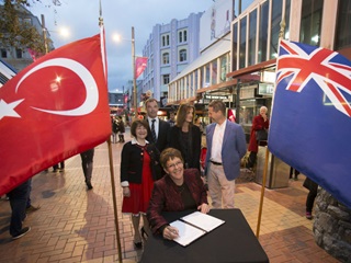 Mayor Celia Wade-Brown signing the Memorandum of Understanding with the Turkish flag on her left and the New Zealand flag on her right.
