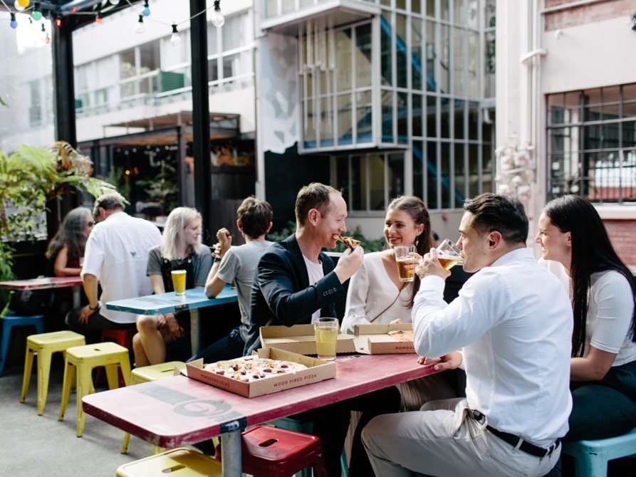 People sitting at tables outside a bar enjoying pizza and beer.