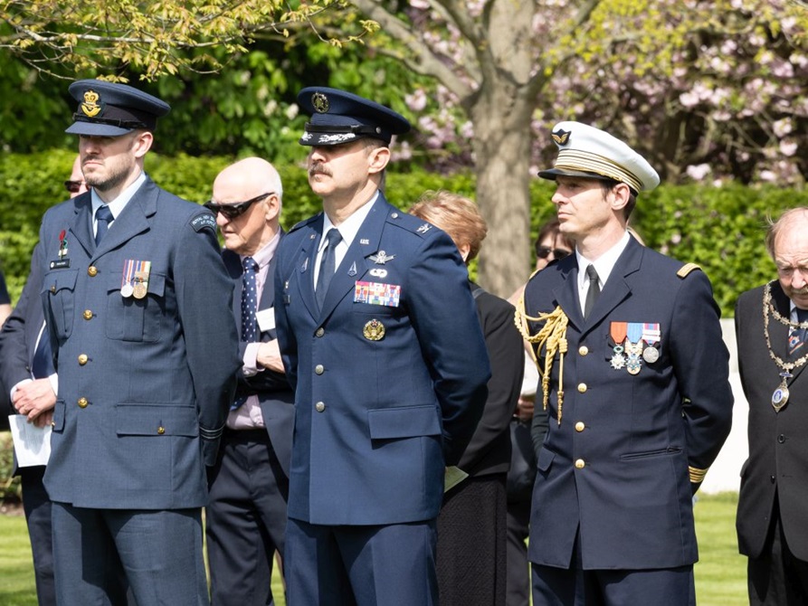 Service members in uniform observe the ceremony with their arms held behind their backs.
