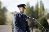 A man in uniform gives a speech from a lectern in front of the war memorial wall.