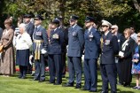 A crowd standing on grass observe the ceremony. Among them are service members in dress uniform.