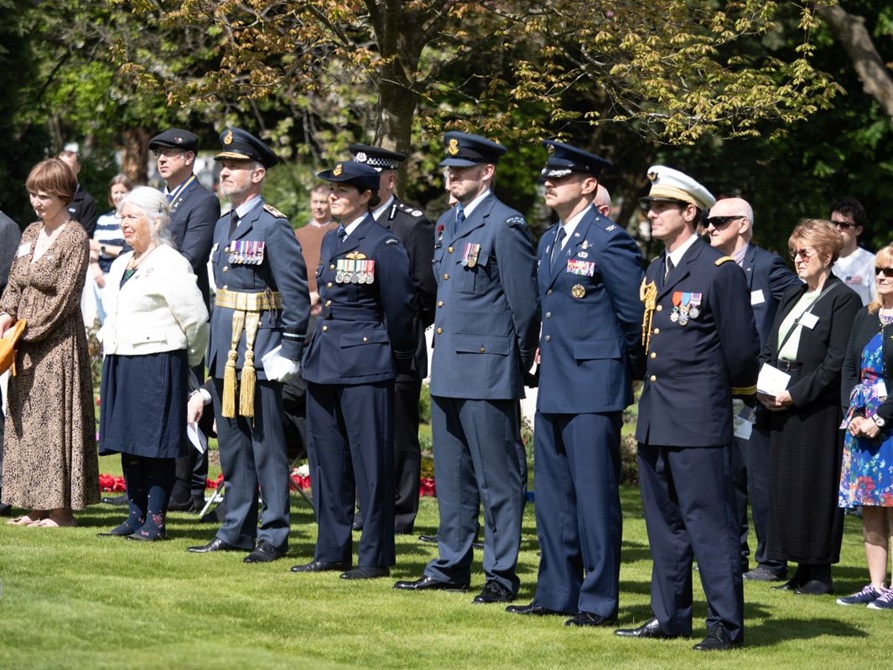 A crowd standing on grass observe the ceremony. Among them are service members in dress uniform.