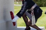 A woman in service uniform lays a poppy wreath at the foot of the Anzac memorial wall.