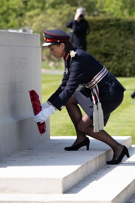 A woman in service uniform lays a poppy wreath at the foot of the Anzac memorial wall.