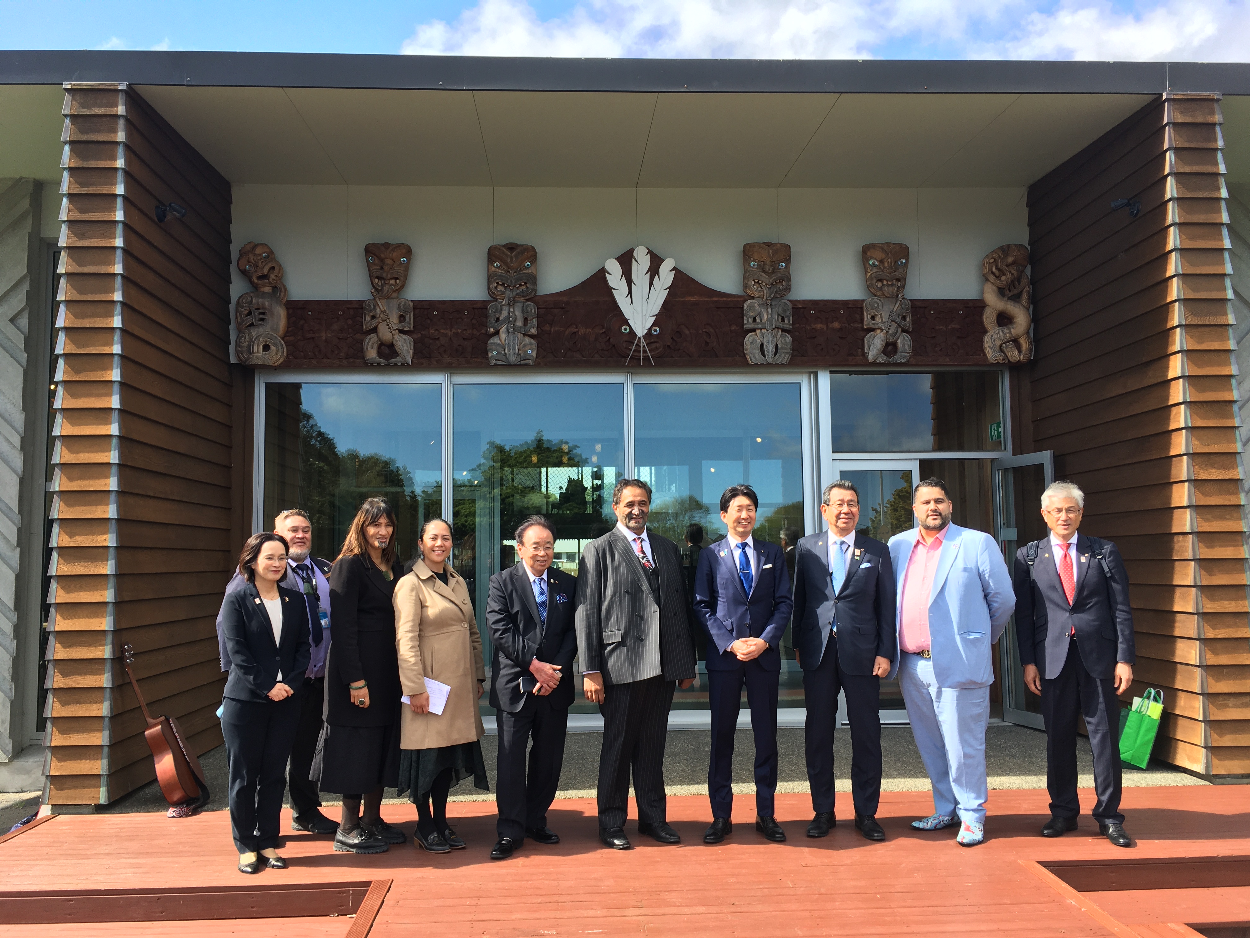 Japanese delegation and members of Te Runanganui standing in front of a building with maori carvings.