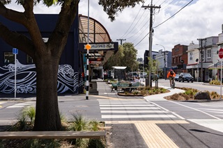 A zebra crossing in Island Bay village after the upgrades. A cyclist is curving a bend on the cycle path.