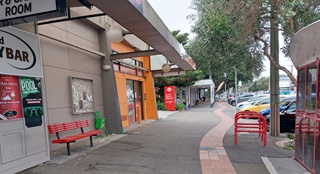 A footpath in Island Bay showing a community notice board on the left and bus stop on the right. The area looks run down.