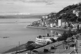 A black and white photo of Oriental Parade shot from behind. It shows the Band Rotunda and a Waka in the harbour.