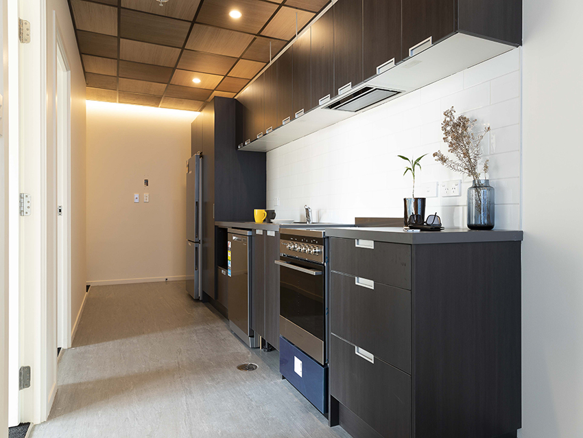 Kitchen at Te Kainga Aroha, showing dark cupboards with silver handles, all modern and clean.