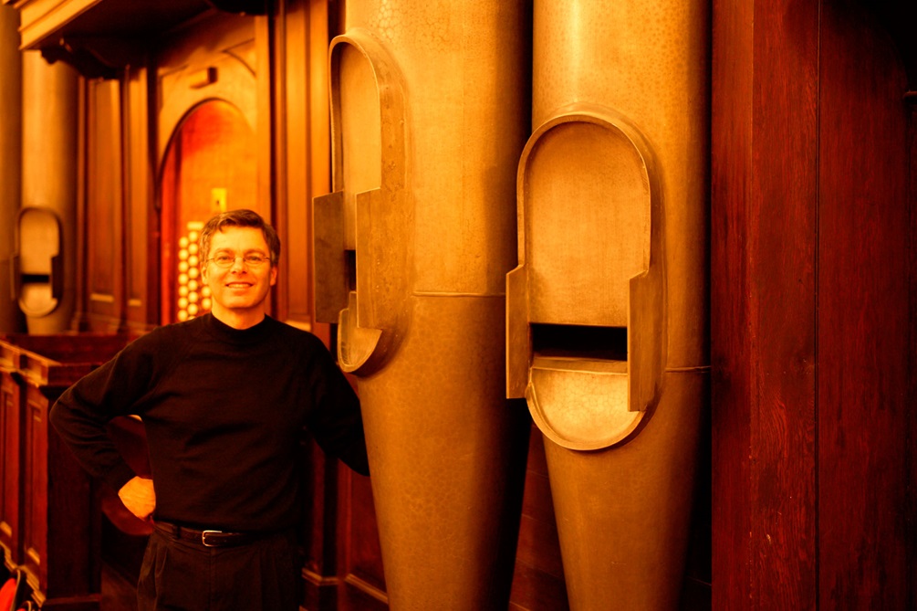 Douglas Mews standing next to Wellington Town Hall organ's great pipes.
