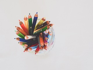 Many coloured pencils arranged in a jar, viewed from above on a neutral white background.