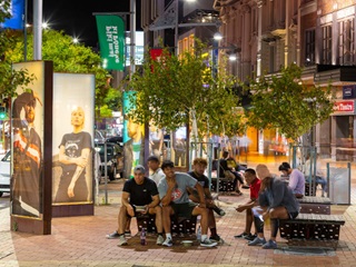 A group of people in Courtenay Place, next to light boxes displaying artwork by Chevron Hassett.