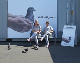 Two people sit in front of a billboard-sized picture of a pigeon.