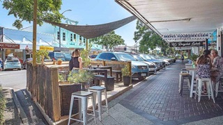 An outdoor dining area in a carpark with tables, chairs and shade.