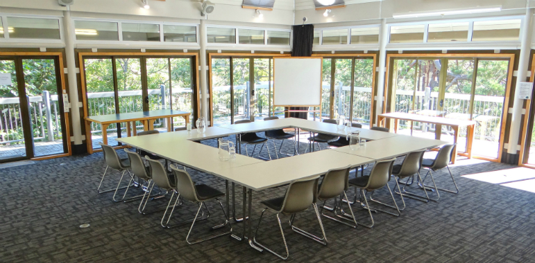 Seminar room with tables and chairs surrounded by windows.