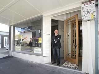 Photo of a man in a blue suit leaning against the front of a shop premises on Cuba St that has been newly renovated and painted white and grey.