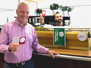 Kevin Lavery standing with the kia kaha cards in a coffee shop.