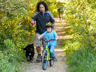 A man walking a dog and a child riding a bike through the bush.