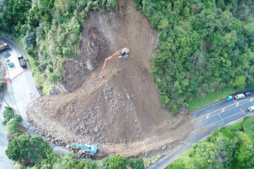A birds eye view photo of a digger on top of a massive slip on Wellington's Ngaio Gorge, which is blocking both lanes of the road.