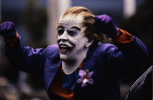 Photograph of a man wearing a creepy Joker mask and purple suit 