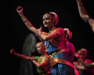 A woman in colourful cultural Indian dress, on stage with other dancers, performing at Diwali.