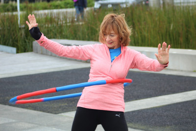 A women in a pink jersey confidently rocking a hula-hoop outdoors. 