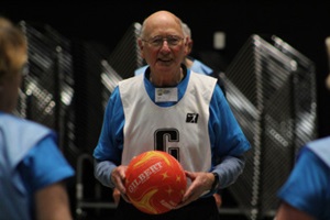 An older man wearing a sports big and holding a ball, ready to get active while smiling at the camera.
