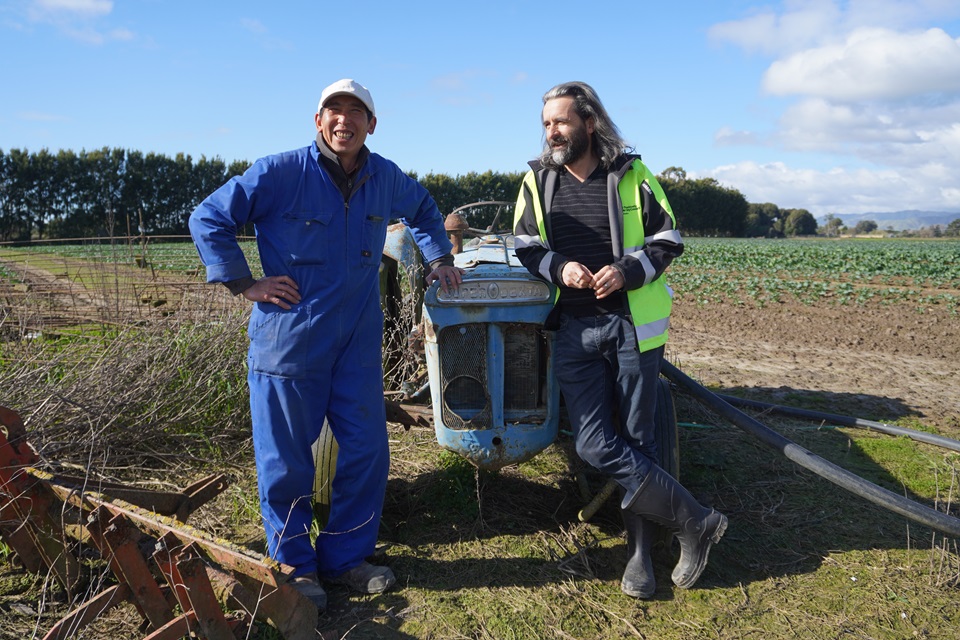 Image of Tony, a produce grower in Levin, with Harbourside Market manager Fraser, standing in a field next to a tractor.