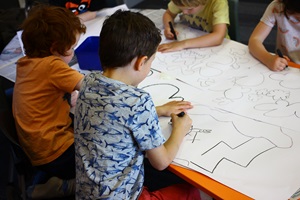 Four children from a Wellington primary school sitting at a table, drawing nature-inspired shapes on large pieces of white paper. These drawings inspired the designs on Wellington City Council's wall murals at Te Awe Library.
