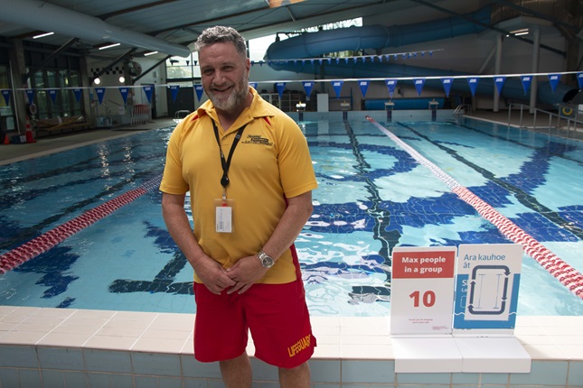 Lifeguard of 25 years, Louie Hoskins, standing in his uniform smiling in front of Karori Swimming Pool.