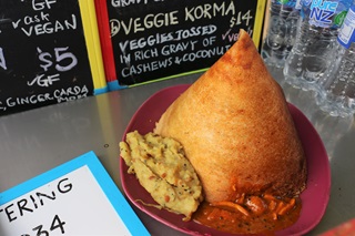 A close-up of a South-Indian masala dosa dish, which is a crunchy golden pancake, artfully rolled up to resemble a tent and placed on a pink plate on top of two tasty curries.
