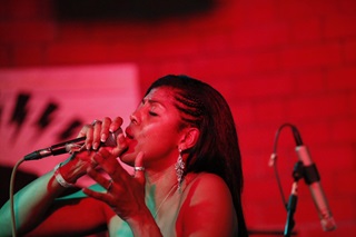 A close-up shot of Colombian salsa singer, Anayibi Loboa Linan singing into a microphone in a red-lit room.