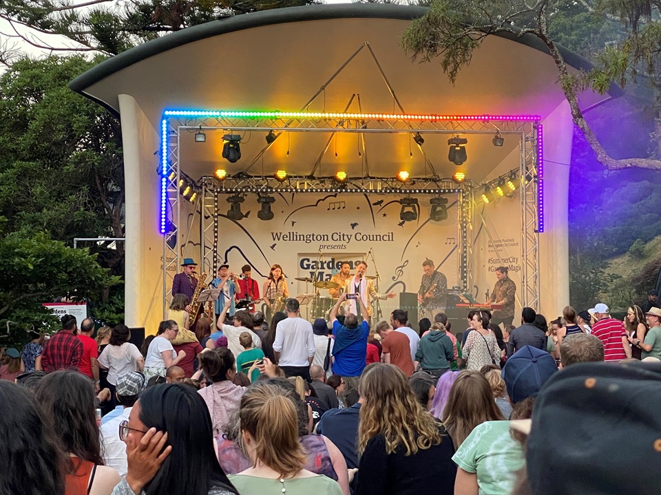 The colourfully lit stage at Gardens Magic with a band performing and a crowd dancing and having a blast.
