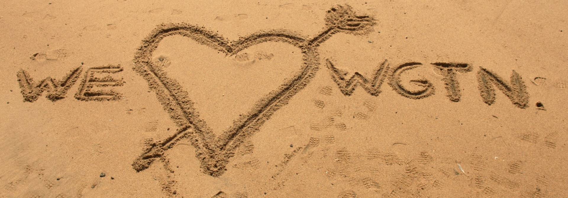 A love heart drawn in the sand with the words 'we' and 'Wellington' written on either side.