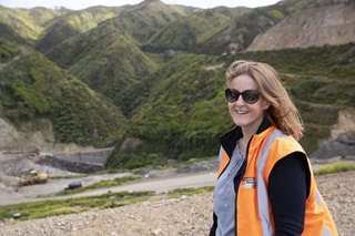 Emily Taylor-Hall, in her high-vis orange vest, smiling with the Southern Landfill and surrounding hills behind her.