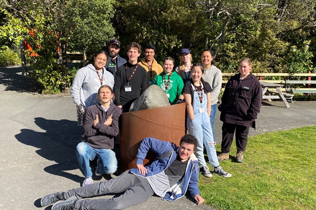Eleven young people standing in a group smiling at the camera. They are members of the Zealandia Youth Collective.