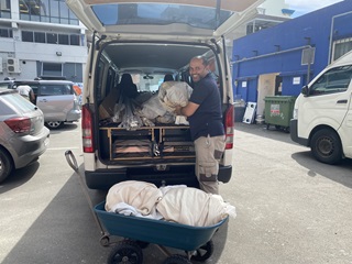 A man happily unloading donated curtains from a white van, and loading them into a wheel barrow to be given to the Sustainability Trust.