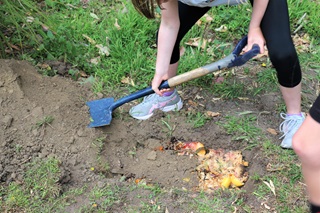 A girl with a space and sneakers, digging dirt over brightly coloured compost on a lawn.